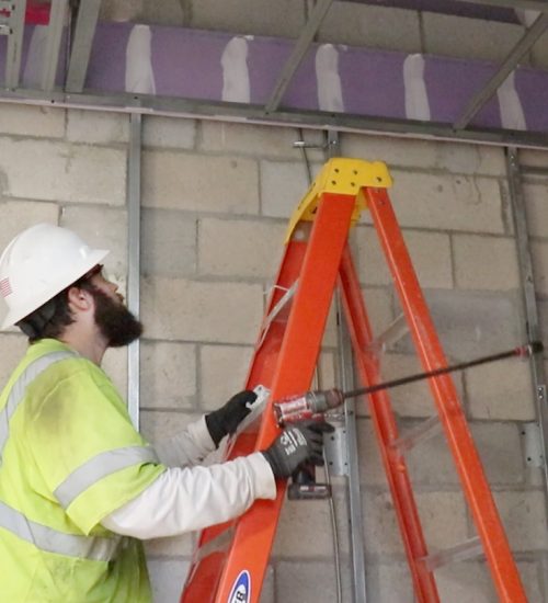 Electrical apprentice on job site climbing a ladder